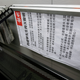 A printed rectangular sign is stuck sideways underneath the bannister of a glass-walled staircase. The paper is printed in black and white and has a statement written in traditional Chinese characters.